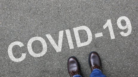 covid-19 Bildet viser et menneske som ser ned på bakken hvor det står covid-19