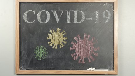 Bildet viser en skoletavle. På tavlen står det skrevet covid-19 og det er tegninger av koronaviruset.