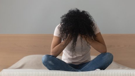 Kvinne alene på en seng med hodet i hendene Bildet viser en kvinne som sitter alene på en seng med hodet i hendene