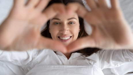 Bildet viser en kvinne som viser et hjertesymbol mens hun ligger i sengen Søvn