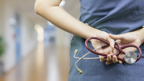 Bildet viser en helsearbeider med hendene på ryggen. Bildet viser en helsearbeider med hendene på ryggen.