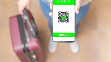 vaksine-pass Bildet viser en kvinne med en koffert som viser, med mobilen sin, at hun er vaksinert for covid-19