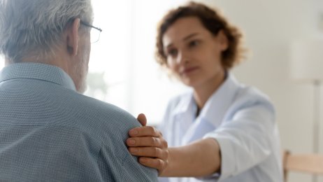 Eldre mann og helsepersonell Bildet viser helsepersonell som legger en trøstende hånd på en eldre mann.