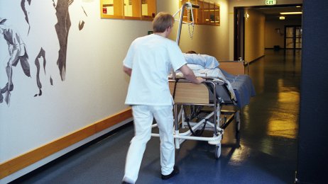 Sykepleier Bildet viser en mannlig sykepleier som triller en pasientseng i sykehus