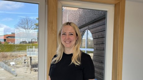 Bildet viser Helene Herlandsen. Hun står foran et vindu og smiler til kamera