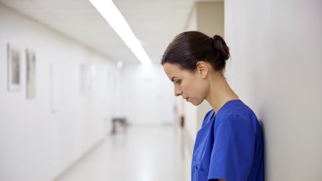 Bildet viser en sykepleier med bøyd hode som lener seg til en vegg. Hun er trist.