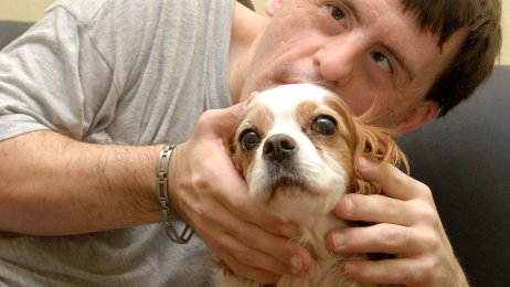 Mann med Downs syndrom stryker på en hund. Mann med Downs syndrom koser med en hund.