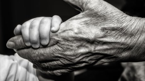 Bildet viser et lite barn som holder et gammelt menneske i hånden.