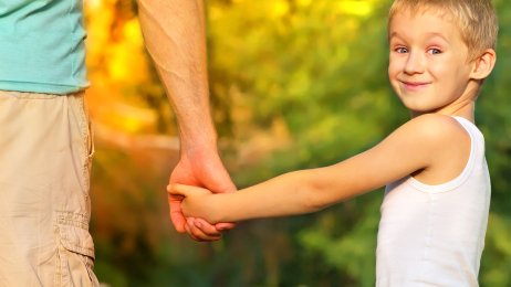 Sønn og far Bildet viser en smilende gutt som holder sin far i hånden