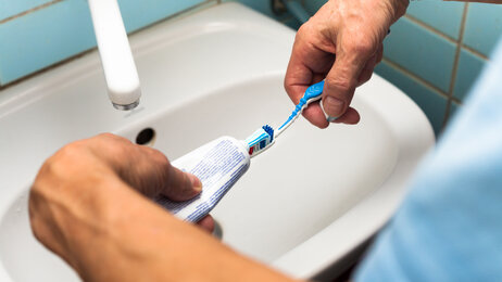 Bildet viser to hender som tar tannkrem på en tannbørste.