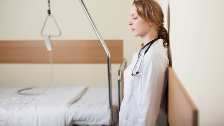 Bildet viser en kvinne - helsepersonell - som er sliten og lener seg inntil en veggen. En sliten sykepleier på en helseinstitusjon.