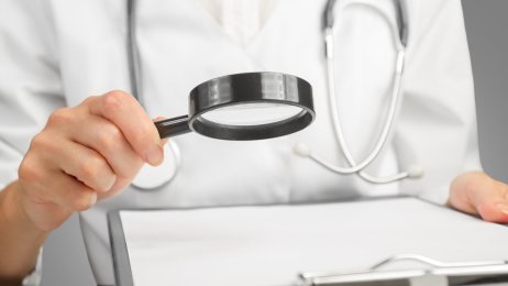 Sykepleier med forstørrelsesglass Bildet viser overkroppen til en sykepleier som holder et forstørrelsesglass