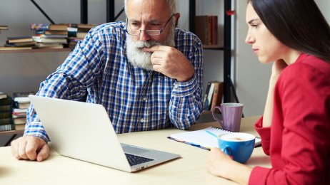 Ung jente og eldre mann ser på en PC Ung jente viser en eldre mann noe på PC-en sin på et kontor
