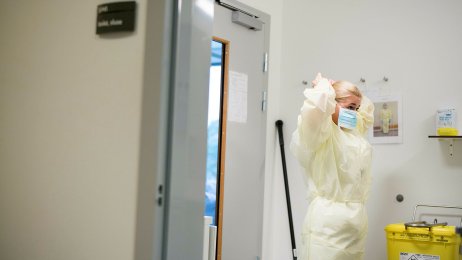 Smittefrakk Bildet viser en sykepleier som står i en sluse inn til et isolat og tar på seg gul smittefrakk.