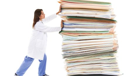 Papirdytter Bildet viser en kvinnelig helsearbeider som dytter på en kjempestor stabel med dokumenter og mapper