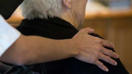 Omsorg for eldre mann Bildet viser en eldre mann sett bakfra, der en omsorgsfull hånd ligger på skulderen hans.