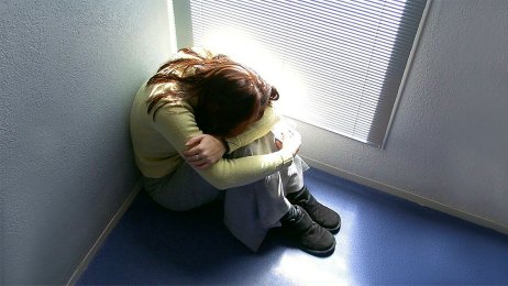 Bildet viser en jente som sitter på gulvet med hodet skjult mellom bena