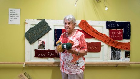 Fosshagen dagsenter i Lier Bildet viser demenssyke Ragnhild på Fosshagen dagsenter i Lier. Hun står foran en tavle med lapper hun har strikket. På lappene står blant annet "alene", "savn" og "ærlig".