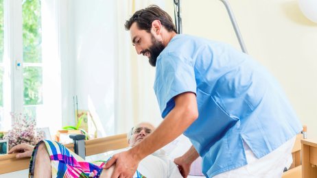 Sykepleier og eldre pasient Bildet viser en eldre mann som blir stelt av en mannlig sykepleier.