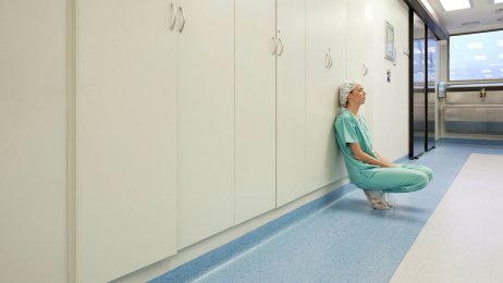 Sliten Bildet viser en pleier som sitter på huk lent mot en vegg og ser sliten ut.