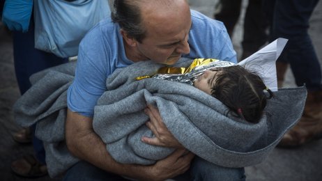 flyktninger, Lesbos Bildet viser en mann med et lite barn inntullet i teppe i armene.