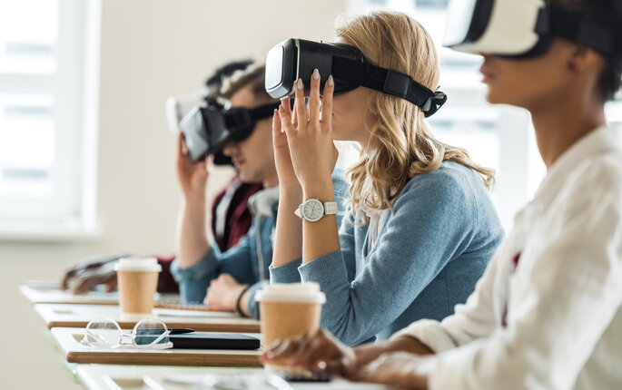 Bildet viser studenter med VR-briller på. De sitter ved sine pulter i et klasserom