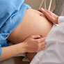 Bildet viser en gravid dames mage. Hendene til en lege eller sykepleier undersøker magen