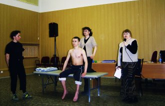 Bildet viser to norske fysioterapeuter som demonstrerer foran et russisk publikum. En mannlig pasient sitter på en seng, mens en tolk oversetter.