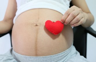 Bildet viser en gravid mage og en hånd som holder et tøyhjerte.