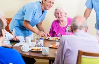 Bildet viser en smilende sykepleier sammen med fornøyde beboere ved et sykehjem.
