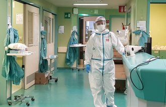 Bildet viser en sykepleier i smittevernutstyr i en sykehuskorridor.