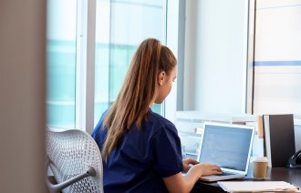 Bildet viser en sykepleier som sitter alene foran pc-en.