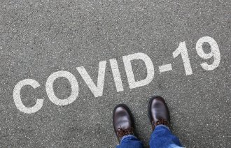 Bildet viser et menneske som ser ned på bakken hvor det står covid-19