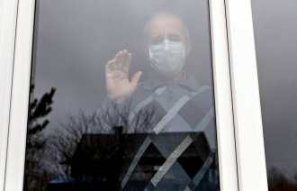 Eldre mann med munnbind bak vindu