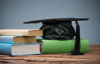 Bildet viser en svart studentlue som ligger på en bokstabel på en gammel trepult