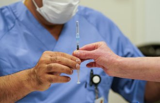 Bildet viser en helsearbeider som gir en ferdig opptrukket koronavaksine til en annen helsearbeider.