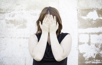 Bildet viser en kvinne som dekker ansiktet med hendene