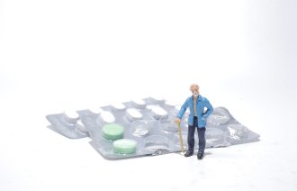 Bildet viser en figur av en eldre mann som står ved siden av et brett med medisiner