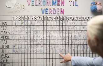 Bildet viser bakhodet på en kvinne foran en tavle med oversikt over fødte barn på fødeavdeling.