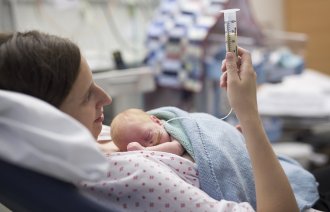 Bildet viser en kvinne på nyfødtintensiven. Hun ligger i sengen og mater sin nyfødte baby ved hjelp av sonde