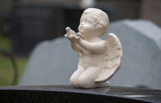 Bildet viser en gravstøtte pyntet med en hvit engel som strekker ut armene.