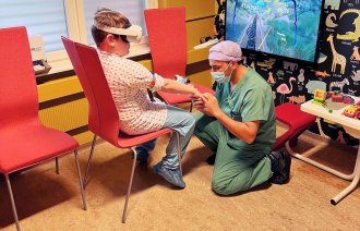 Bildet viser en gutt som har på VR-briller mens en anestesisykepleier legger inn perifert venekateter