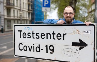 Bildet viser Daniel Kendrick ved et skilt som viser veien til teststasjonen.