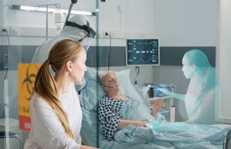 Bildet viser en sy covid-pasient i en sykeseng. En sykepleier i fullt smittevernutstyr står ved siden av. Utenfor vinduet kikker en pårørende kvinne inn, og skyggen av henne kan skimtes ved siden av sengen.