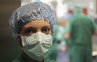 Bildet viser en sykepleier med munnbind foran en operasjonssal