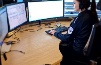 Bildet viser en AMK-sykepleier på AMK-sentralen. Hun sitter foran fire store skjermer og svarer på 113-samtaler