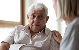 Mann med demenssykdom En kvinnelig sykepleier holder hånden på skulderen til en mann med demenssykdom