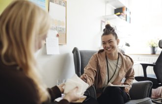 Bildet viser en smilende, kvinnelig helsesykepleier i samtale med en annen kvinne.