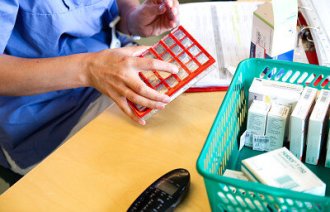 Hjemmesykepleier legger medisiner oppi en dosett.