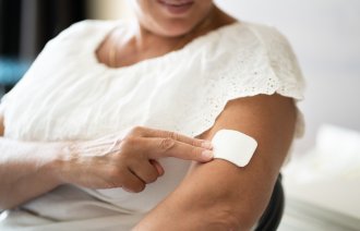 Bildet viser en kvinne som setter på et østrogen-plaster på overarmen.